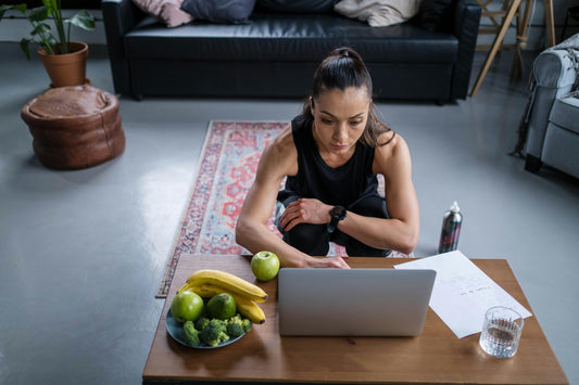 Woman researching home workout gear comparisons on laptop, reading about HupSix vs TRX, Peloton, and Tonal for smarter at-home fitness decisions