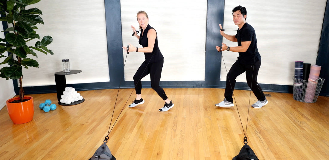 Two people doing a HupSix interval cardio workout in a small home studio, guided by music and movement.