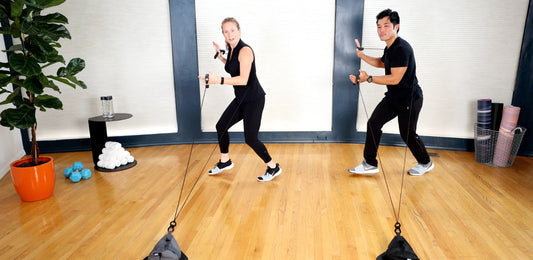 Two people doing a HupSix interval cardio workout in a small home studio, guided by music and movement.